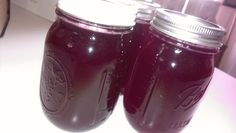 two mason jars filled with purple liquid sitting on a counter next to a person's hand