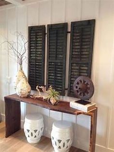 two white vases sitting on top of a wooden table in front of shuttered windows