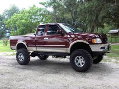 a red pick up truck parked on top of a dirt road in front of trees