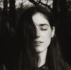 a black and white photo of a woman with her eyes closed in front of trees