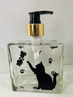 a glass soap dispenser with a cat design on the front and paw prints on the back