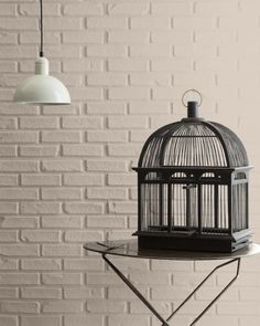 a birdcage sitting on top of a table next to a white brick wall