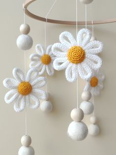 white and yellow crocheted flowers hanging from a wooden rod with balls attached to it