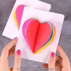 someone is holding up a heart shaped card with colored strips on it and the paper has been folded in half