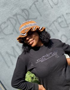 a woman wearing a black shirt and a brown knitted hat is standing in front of a wall with writing on it