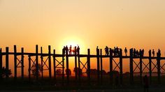 people are standing on the wooden bridge at sunset