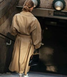 a woman is walking down the stairs in a trench coat