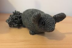 a crocheted gray stuffed animal laying on top of a wooden table next to a white wall