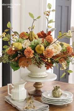 an arrangement of flowers in a white vase on a table with plates and silverware