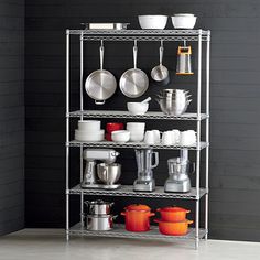 a metal shelving unit with pots and pans on the top shelf in front of a black wall