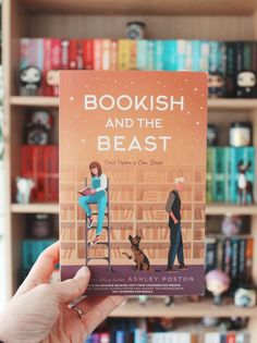 a person holding up a book in front of a bookshelf