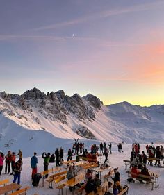 a group of people standing on top of a snow covered slope next to benches and tables