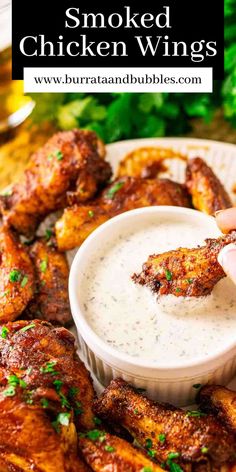 someone dipping chicken wings into a white bowl with ranch dressing on the side and garnished with parsley