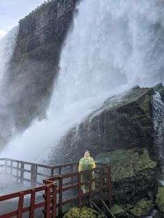 a person standing on a bridge in front of a waterfall with water pouring over it