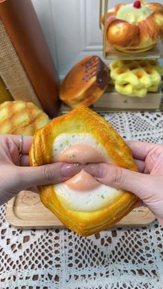 a person holding an egg in a bread bun with other pastries on the table