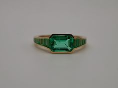 At the centerpiece of this lab grown Colombian emerald ring is a radiant 1.5 ct emerald, set east west to highlight its natural allure. Flanking it are calibre cut emeralds, each uniquely shaped to create a seamless gradient effect, making every ring truly one-of-a-kind. Set in luxurious 18K yellow gold, this ring exudes timeless charm. What makes it truly special? Calibre cut stones are individually shaped to fit precisely into the design, resulting in a mesmerizing display of color and brillia Heirloom Emerald Ring Baguette Cut, Heirloom Style Baguette Cut Emerald Ring, Heirloom Baguette Cut Emerald Ring, Baguette Cut Emerald Ring For May Birthstone, Timeless Baguette Cut Green Emerald Ring, Timeless Emerald Ring With Radiant Cut, Timeless Baguette Cut Emerald Ring Gift, Timeless Green Baguette Cut Emerald Ring, Timeless Green Baguette-cut Emerald Ring