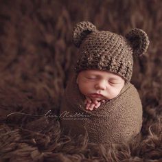 a newborn baby wearing a brown bear hat and sleeping on some fur with it's eyes closed