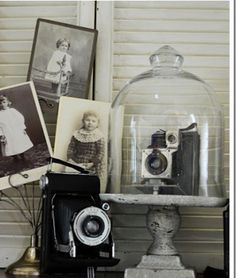 an old fashioned camera sitting on top of a table next to pictures and a glass dome