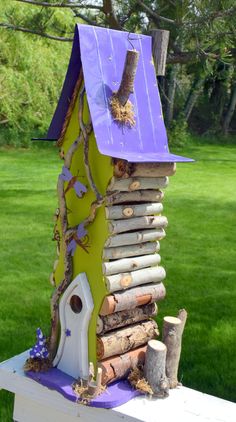 a birdhouse made out of logs and branches on a table in the grass, with a purple roof