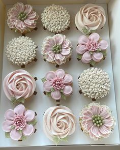 twelve cupcakes in a box decorated with pink and white frosting flowers on top