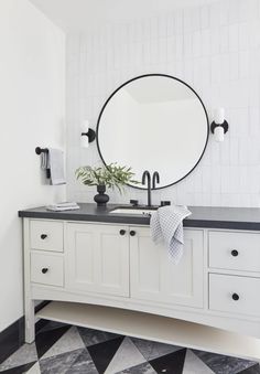 a black and white bathroom with a round mirror on the wall above the vanity area