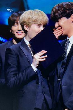 two young men in suits are holding up a piece of black paper to their face