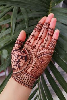 a person's hand with henna on it and palm leaves in the background