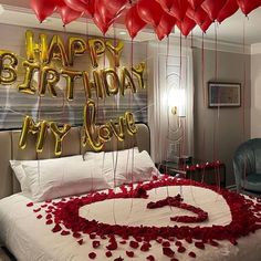 a bed with red rose petals and balloons in the shape of a heart