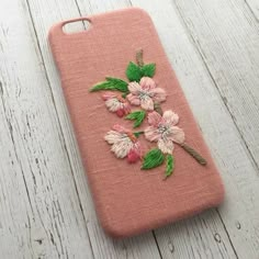 an iphone case with flowers on it sitting on a wooden table next to a white wall