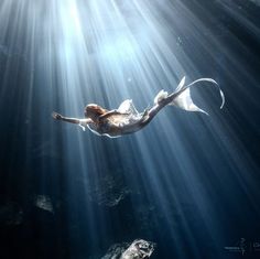 a woman is swimming in the ocean with sunlight streaming through her hair and body,