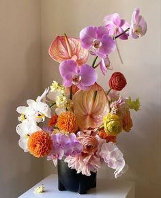 a vase filled with lots of colorful flowers on top of a white table next to a wall