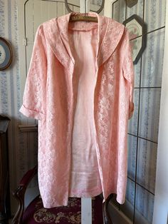 This lovely long jacket is made from gorgeous pink floral lace over a lightweight layer of matching pink satiny fabric. It has a wide collar and an open front with no buttons or snaps. The measurements, taken with the coat lying flat, are: shoulder to shoulder, 14 inches; armpit to armpit, 22 inches; sleeves, 17 inches; length, 37 inches; bottom edge, 26 inches. In very good condition. Feminine Spring Wedding Outerwear, Elegant Pink Daywear Outerwear, Vintage Pink Robe For Spring, Long Pink Robe For Wedding, Long-sleeved Pink Vintage Robe, Fitted Long Sleeve Pink Robe, Pink Fitted Long Sleeve Robe, Fitted Lace Trim Robe For Spring, Long Pink Robe For Spring