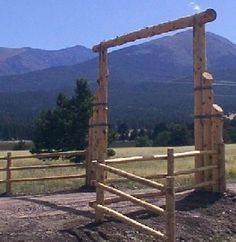 a wooden gate in the middle of an open field with mountains in the background,