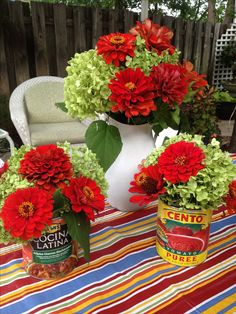 red and green flowers are sitting in buckets on a striped tablecloth with a white chair behind them