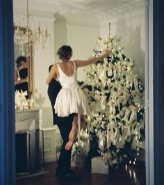 a woman is decorating a white christmas tree