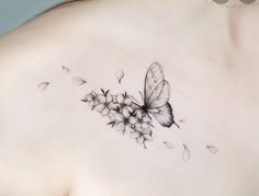 a woman's back with a butterfly tattoo on her shoulder and flowers in the foreground