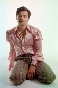 a man sitting on the ground with his hands in his pockets and wearing a pink shirt