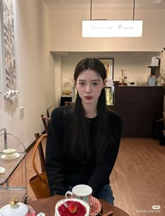 a woman sitting at a table with plates and cups on it, looking into the camera