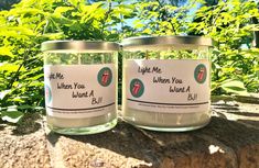 two glass jars with labels on them sitting on a rock in front of some plants