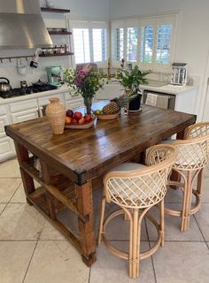 a wooden table sitting in the middle of a kitchen next to two wicker chairs