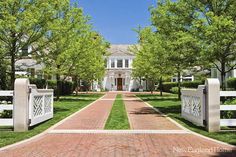 a large white house surrounded by lush green trees and grass with two gates leading to the front yard