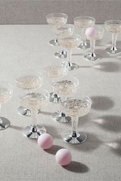 there are many wine goblets with pink balls on the table top and one is empty