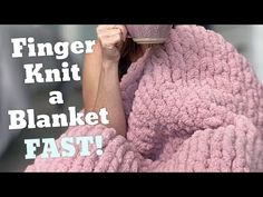 a woman wrapped in a pink blanket holding a coffee cup with the words finger knit a blanket fast