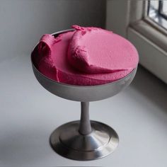 a pink cake sitting on top of a metal plate next to a window sill