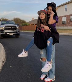 two girls standing in the middle of a street talking on their cell phones and one is holding another girl