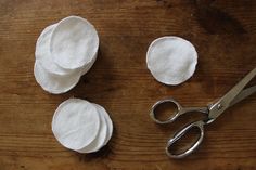 three pieces of white cloth sitting next to scissors on a wooden table with one piece cut out