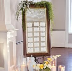 a table with flowers and candles on it in front of a large mirror that is hanging from the wall