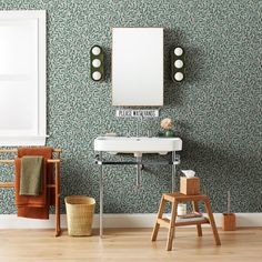 a bathroom with a sink, mirror and stool in front of a wallpapered background