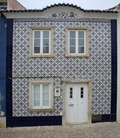 a blue and white building with two windows next to a brick sidewalk in front of it