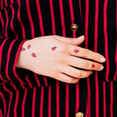 a woman wearing a red and black striped shirt with small tattoos on her left hand